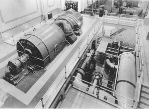 Parsons #1 with generator/exciter in foreground and turbine and control panel in background. Cooling water lines in lower level to the right of generating unit.